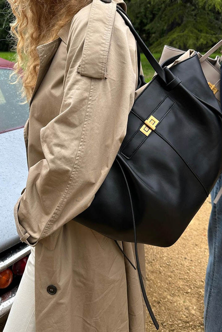 Black leather tote bag on shoulder, worn outdoors over trench coat