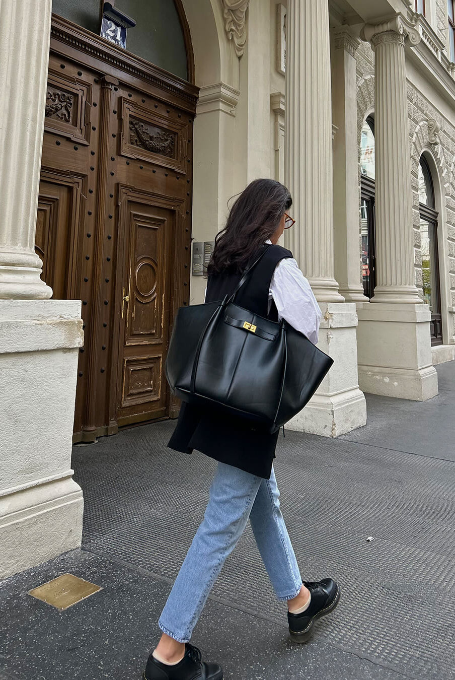 Black leather tote bag on shoulder, model walking outdoors, back view