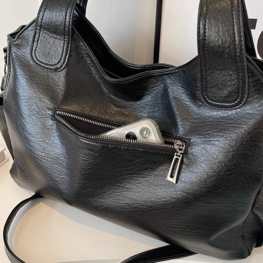Midnight black leather shoulder bag, close-up of the front zip pocket