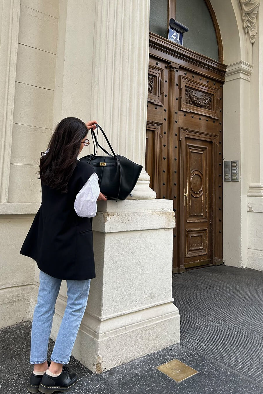 Black leather tote bag carried on shoulder, model outdoors near doorway