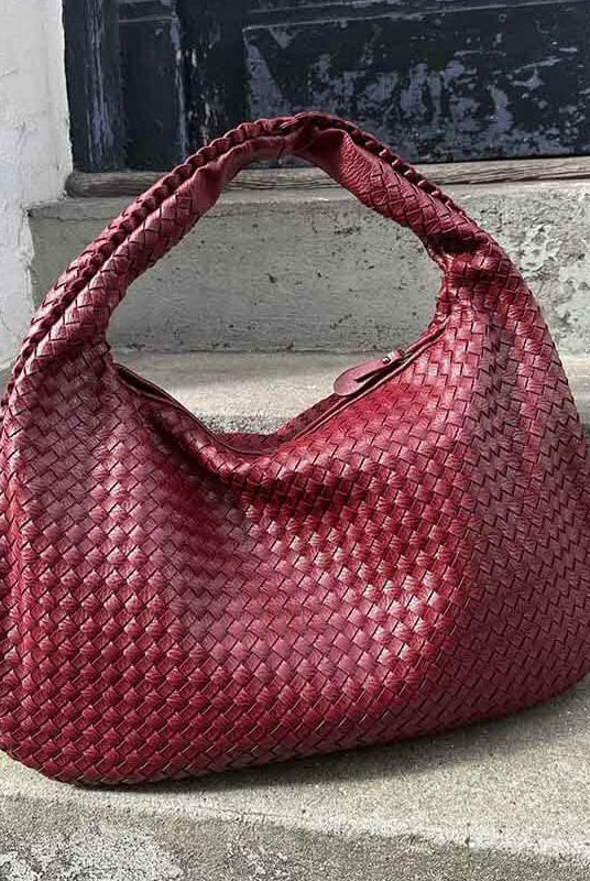 Burgundy woven leather hobo bag resting on stone steps outdoors