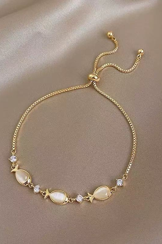 Gold bracelet with opal fish charms and crystals, flat lay on satin