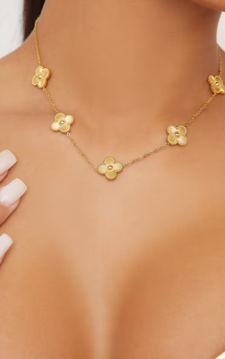 Gold clover-charm necklace, close-up worn on model's neckline