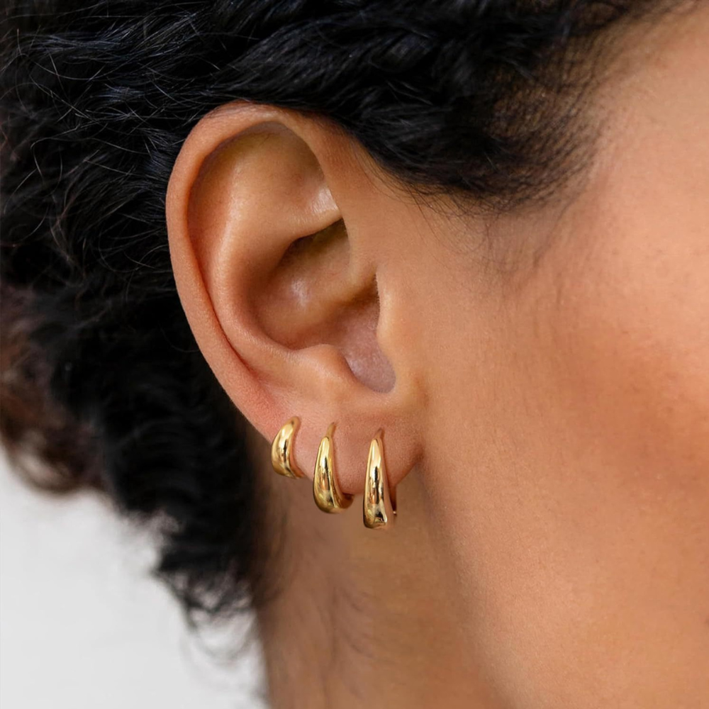Close-up of gold huggie hoop earring trio on model's ear, curly hair