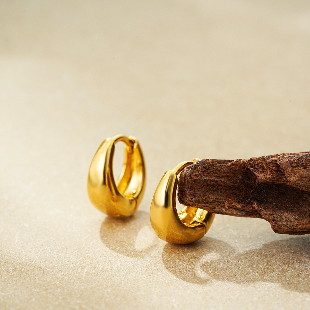 Pair of gold huggie hoop earrings on sand with driftwood