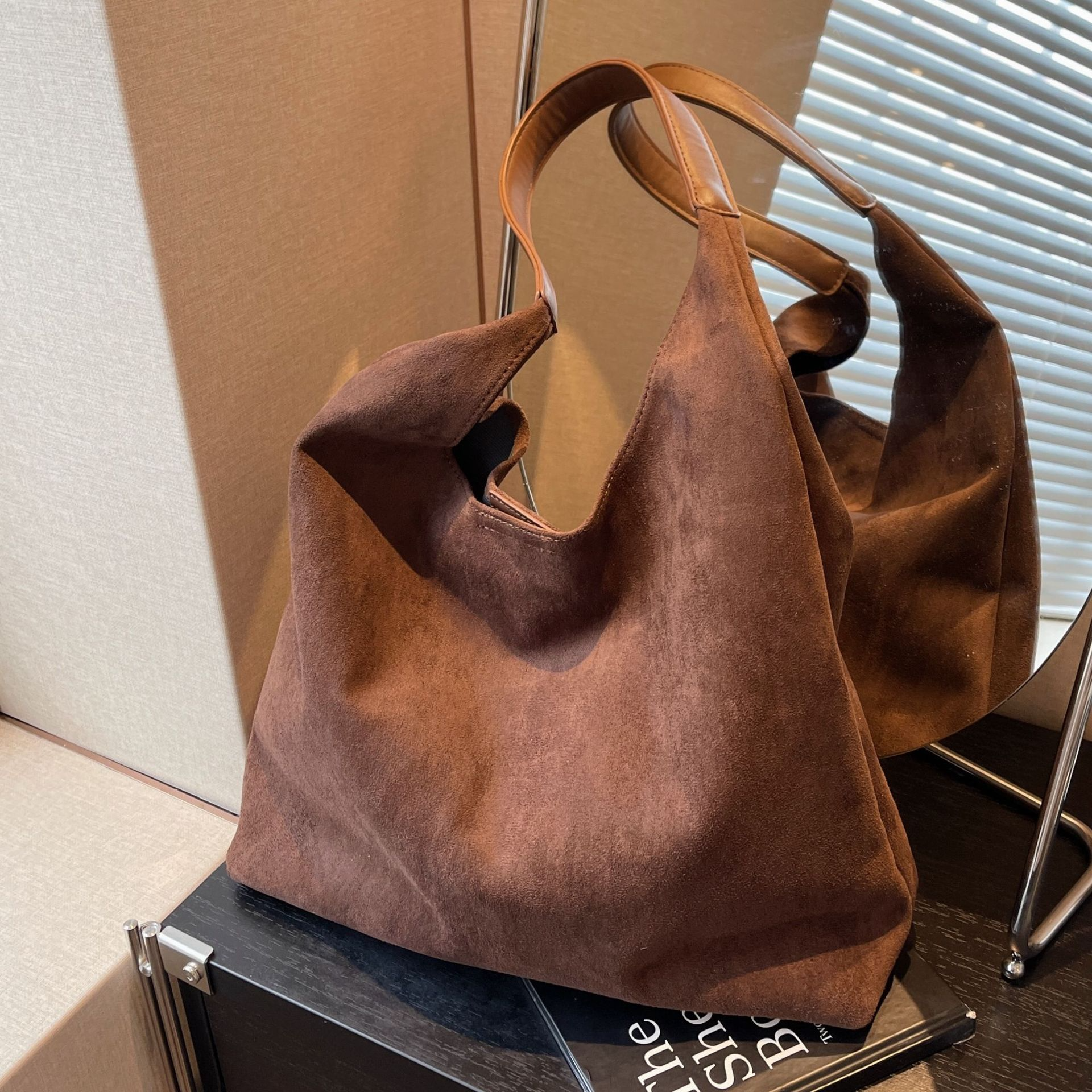 Coffee brown suede tote bag beside a mirror, close-up