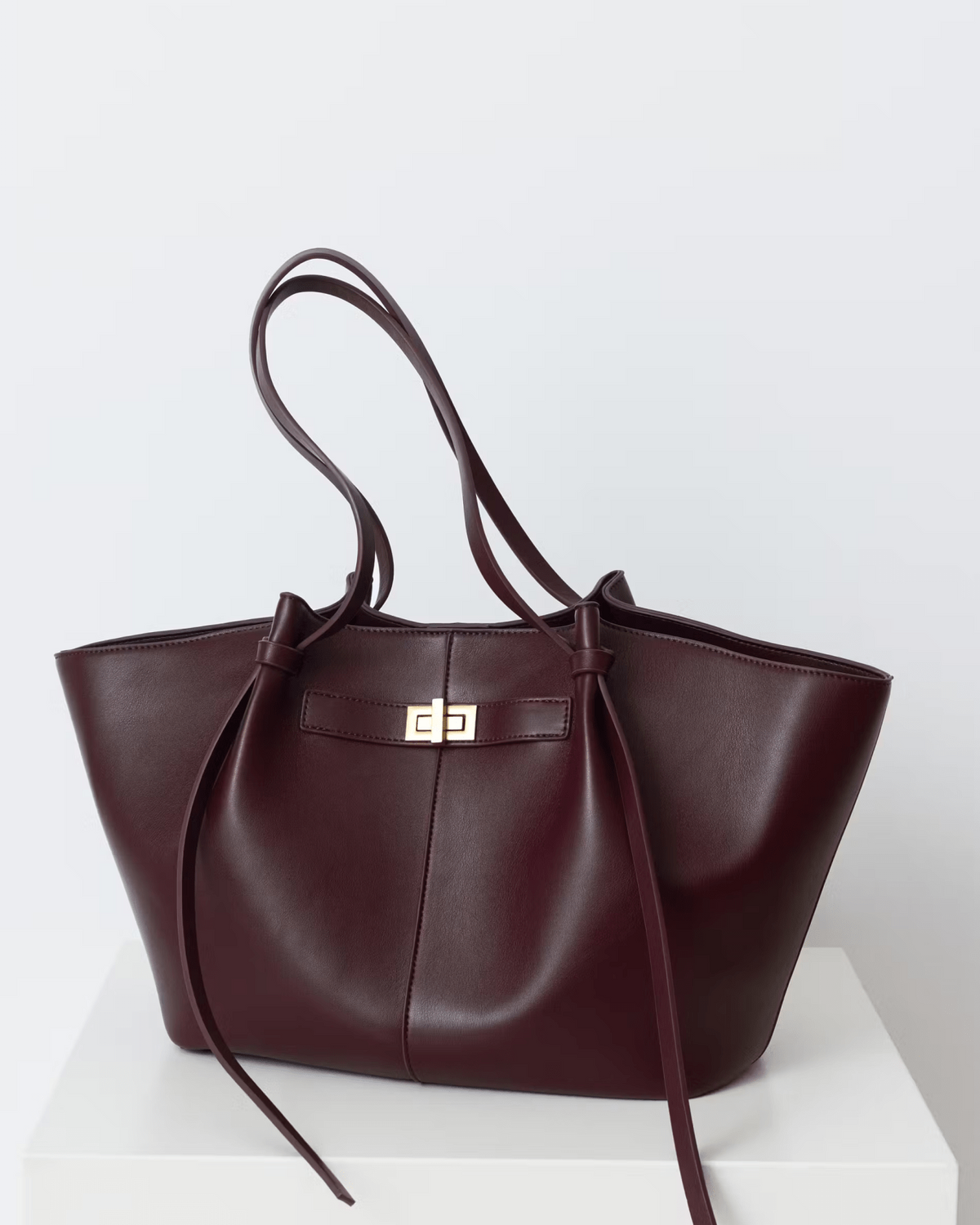 Burgundy leather tote bag with twist-lock strap detail, front view