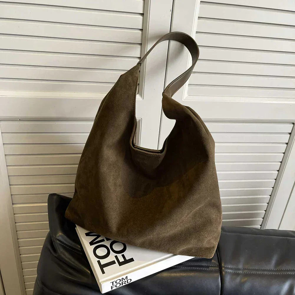 Green suede shoulder tote bag resting on a book