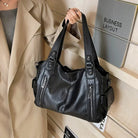 Midnight black leather shoulder bag held by handles on model