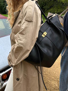 Black leather tote bag on shoulder, worn outdoors over trench coat