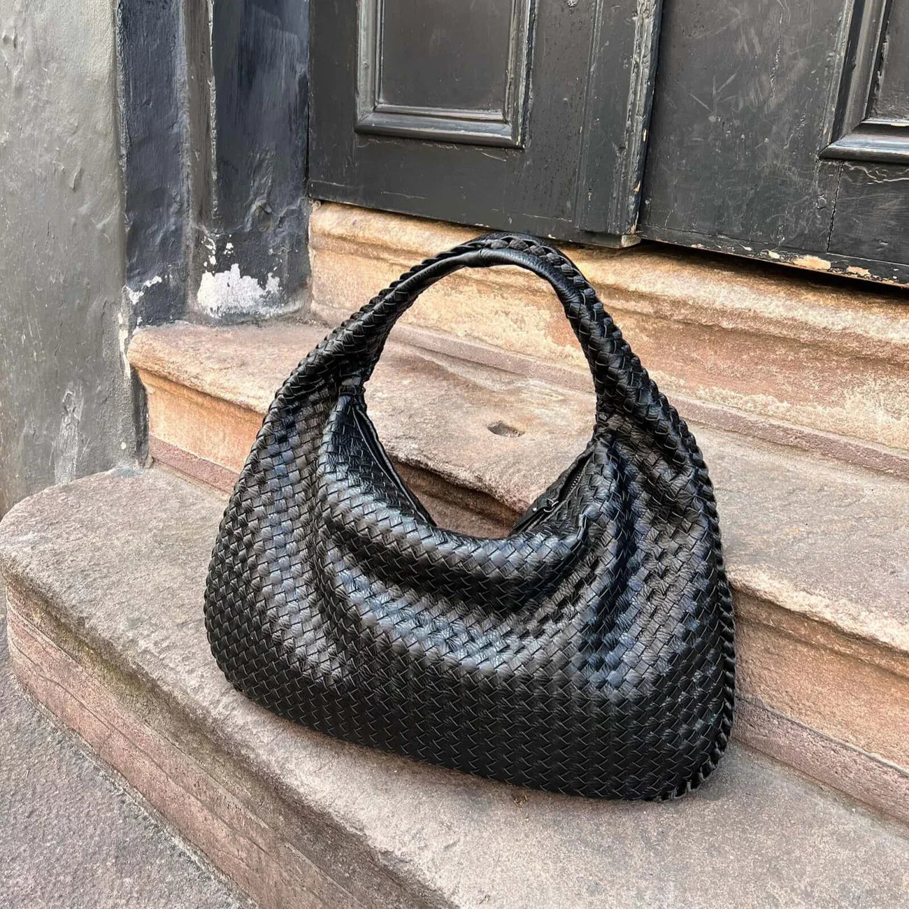 Black woven leather hobo bag resting on stone steps outdoors