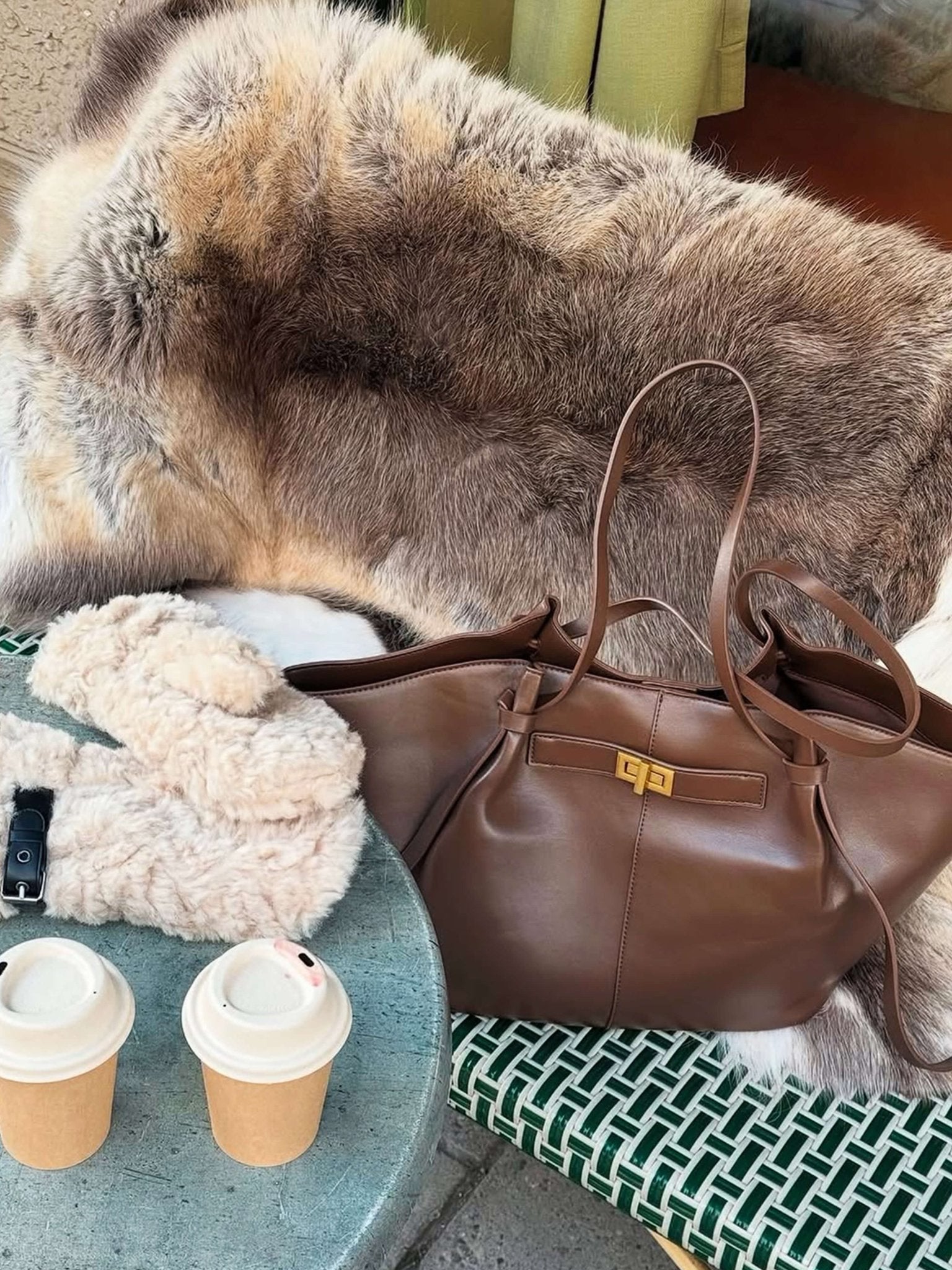 Chocolate brown leather tote bag resting on fur chair, styled flat lay