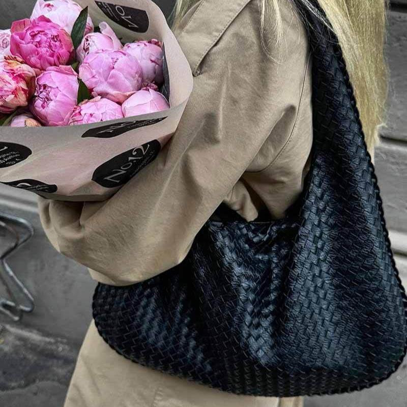 Black woven leather hobo bag on shoulder, model holding flowers