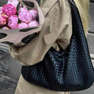 Black woven leather hobo bag on shoulder, model holding flowers