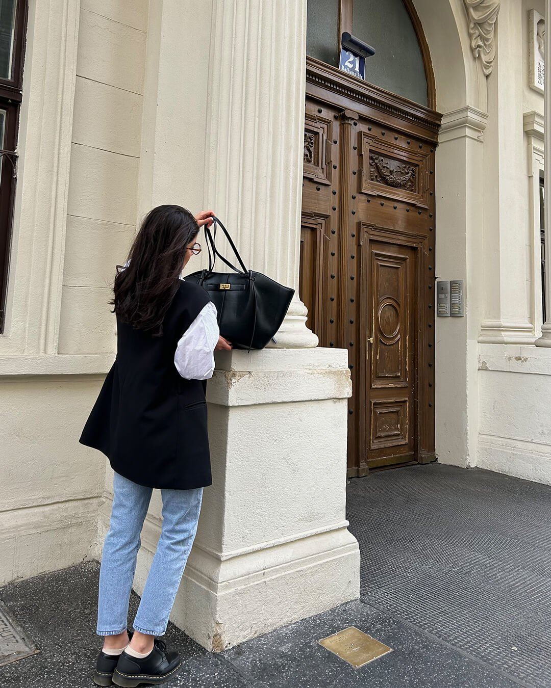 Black leather tote bag carried on shoulder, model outdoors near doorway