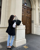 Black leather tote bag carried on shoulder, model outdoors near doorway