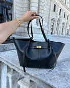 Black leather tote bag held by handles, outdoors on stone ledge
