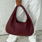 Close-up of burgundy woven leather hobo bag held by handle