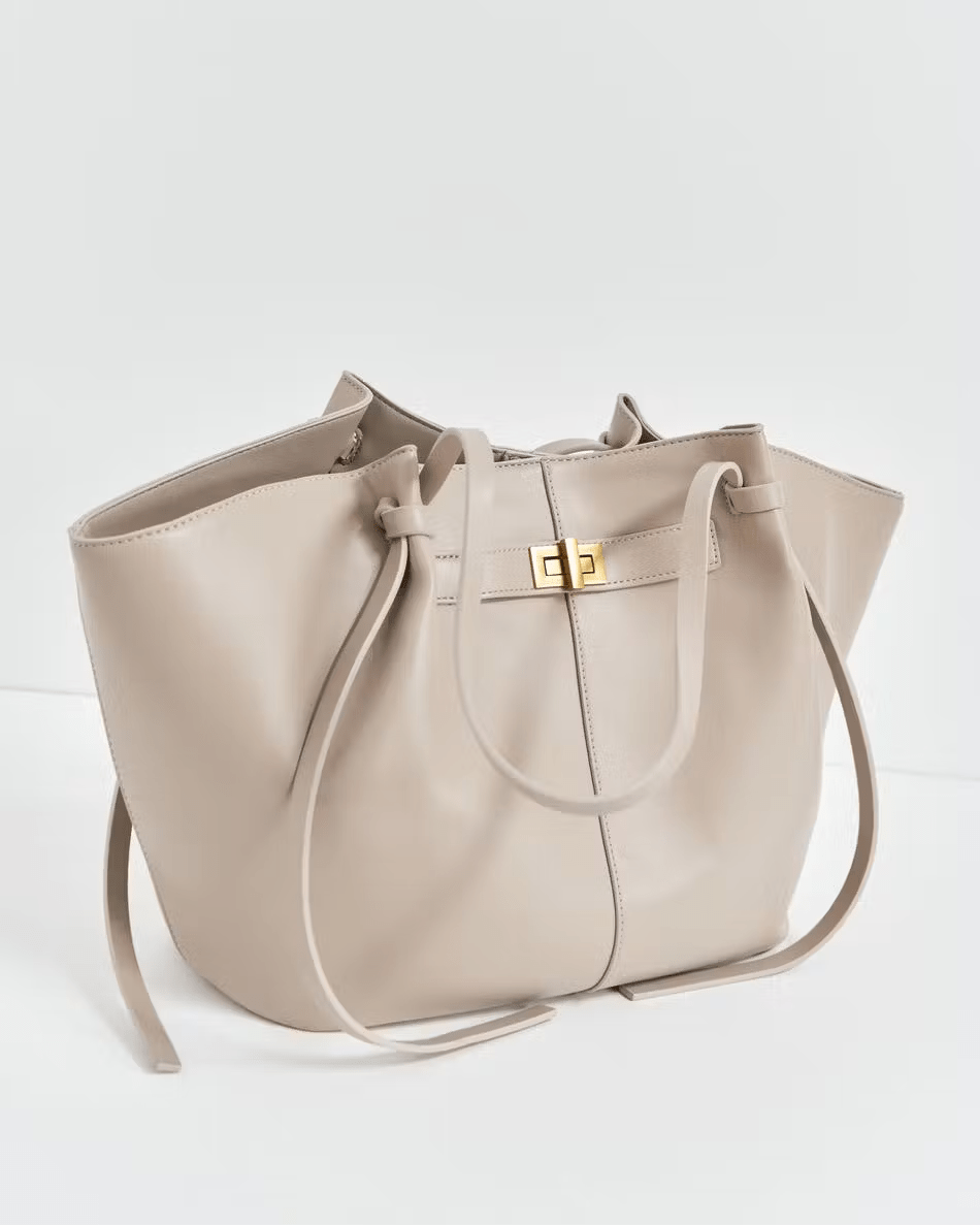 Beige leather tote bag with twist-lock strap detail, angled front view