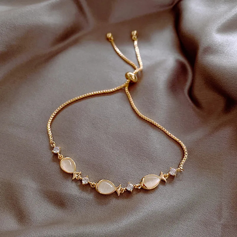 Gold bracelet with opal fish charms, close-up flat lay on dark satin