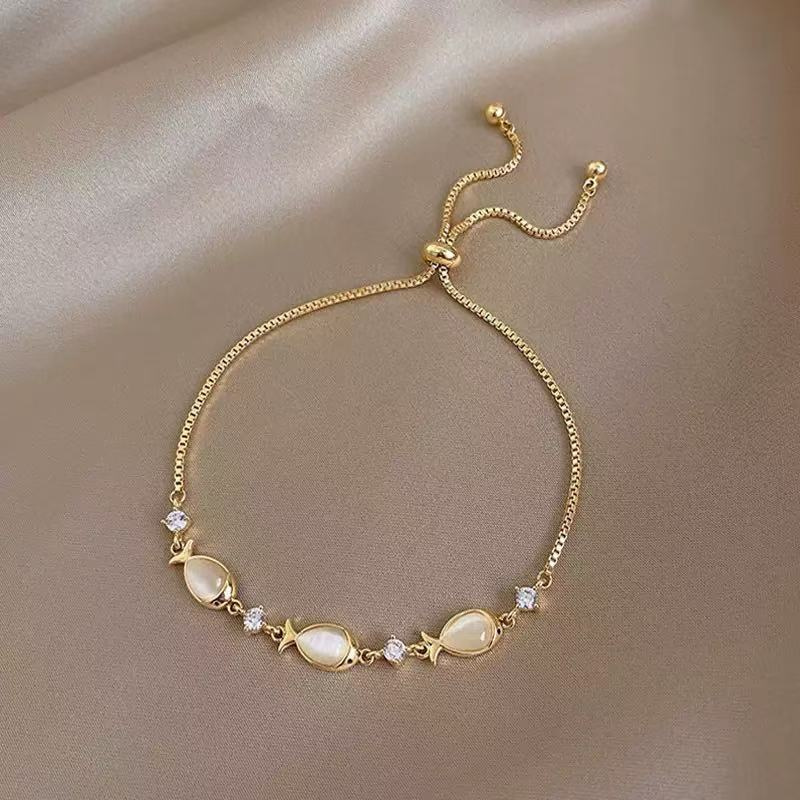Gold bracelet with opal fish charms and crystals, flat lay on satin