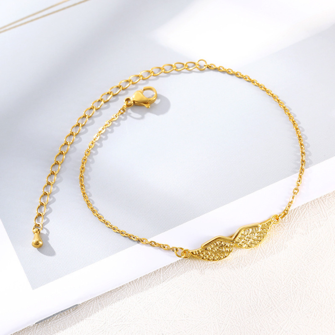 Gold angel wing bracelet, styled flat lay on textured surface