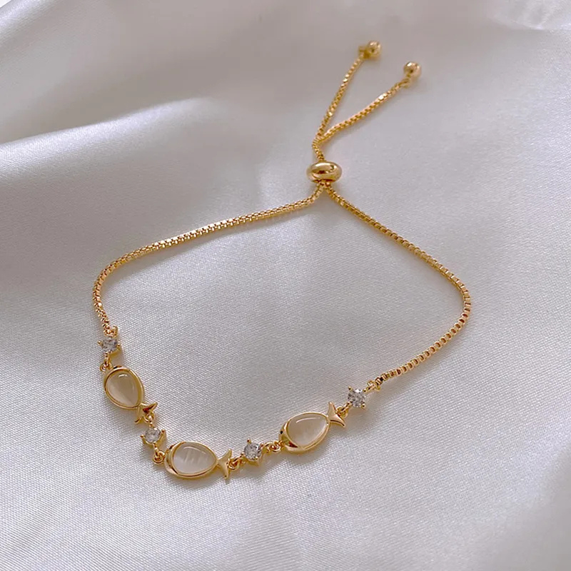 Gold bracelet with opal fish charms, close-up flat lay on white satin