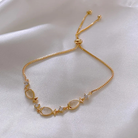 Gold bracelet with opal fish charms, close-up flat lay on white satin