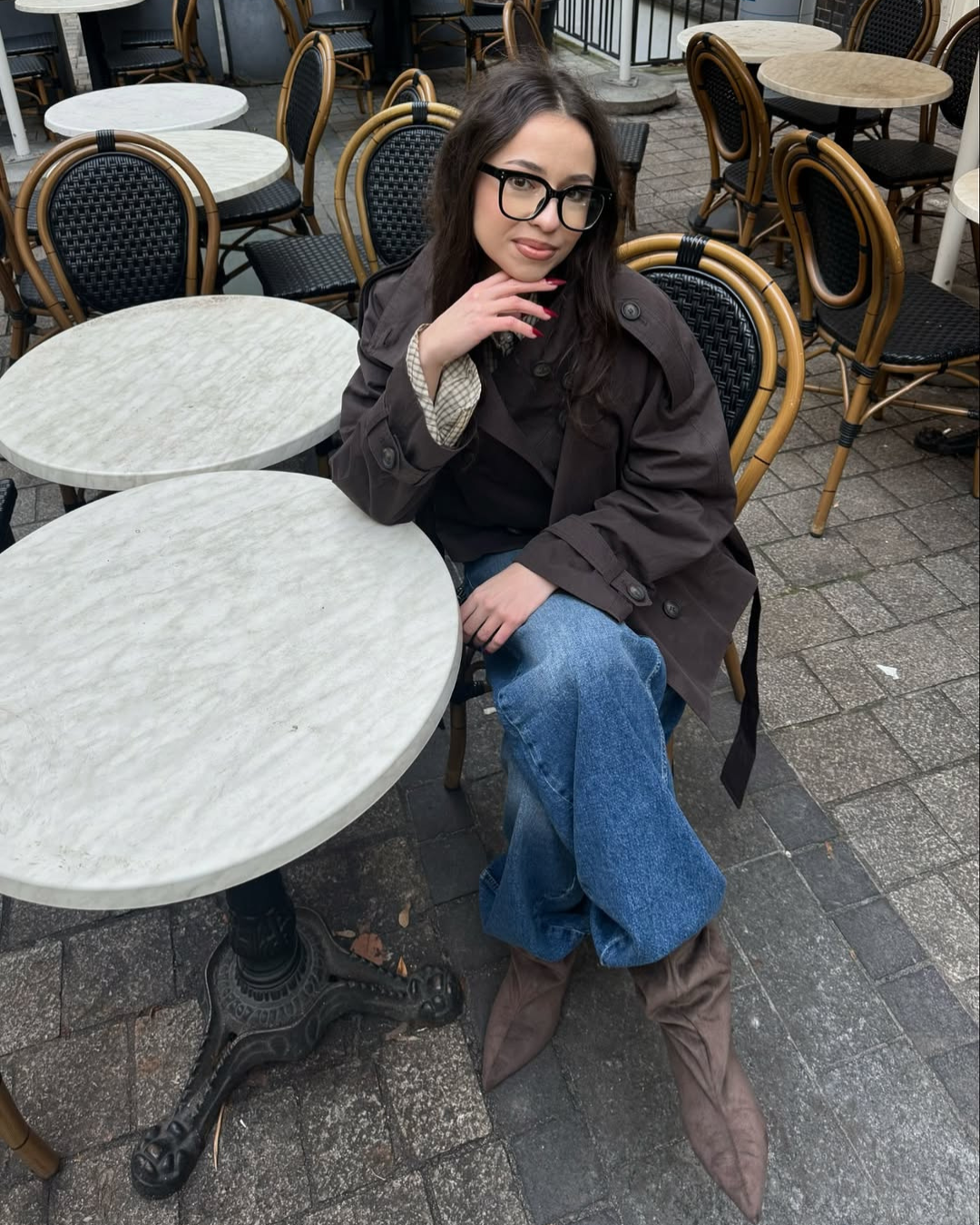 Brown short trench coat, model seated at cafe table, front view