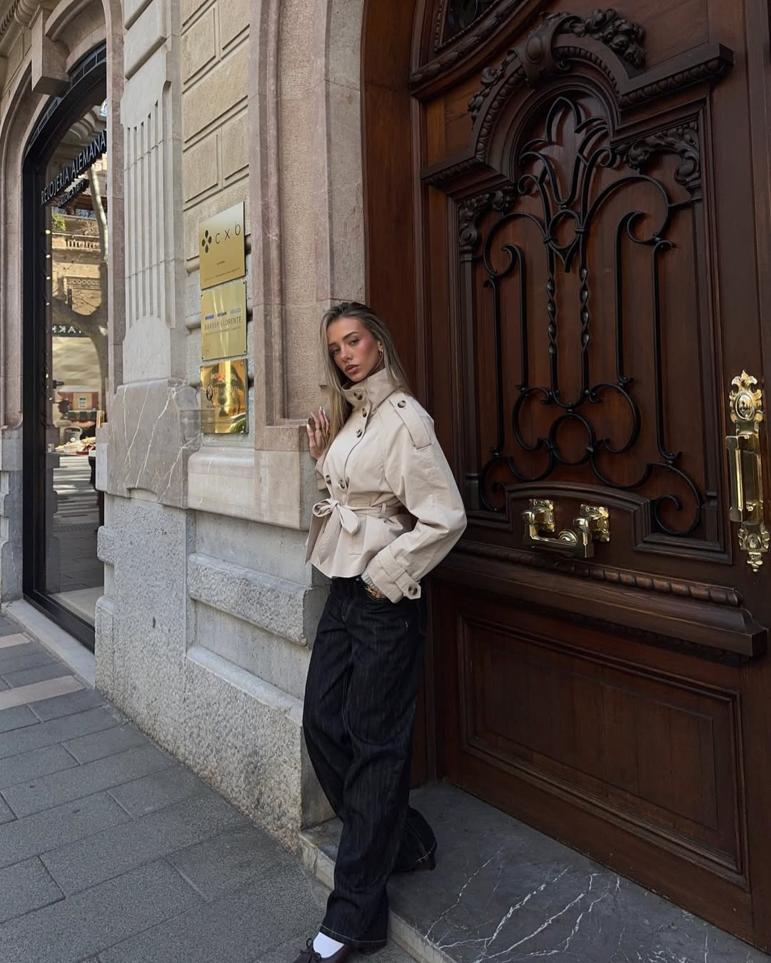 Sand short trench coat, model leaning against doorway, side view