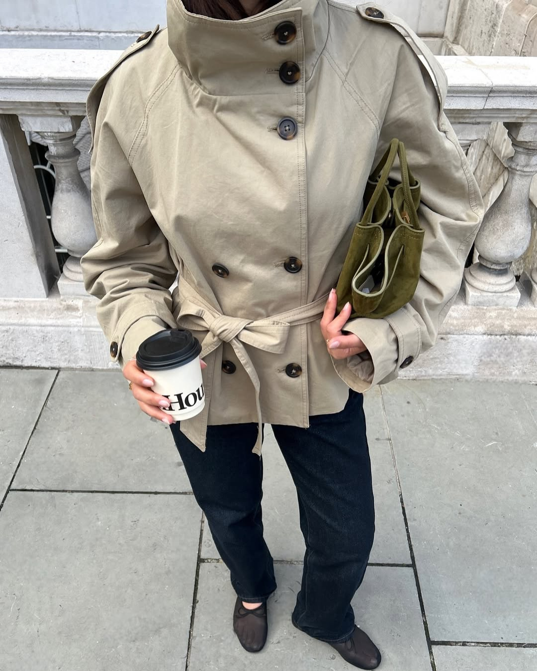 Beige short belted trench coat, close-up with coffee cup