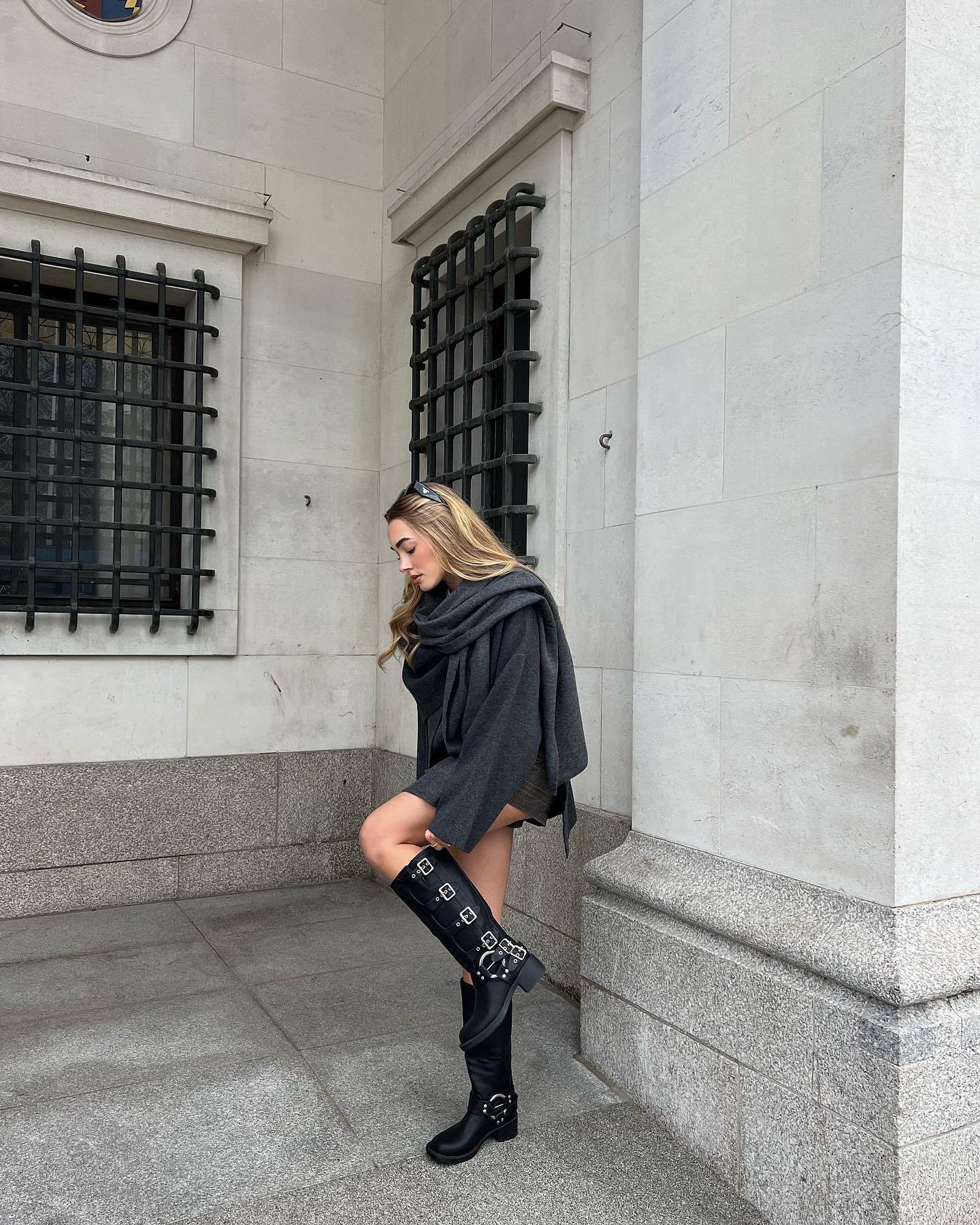 Charcoal short cape with scarf detail, side view leaning on wall