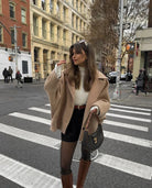 Beige oversized coat over white jumper and black skirt, crossing street