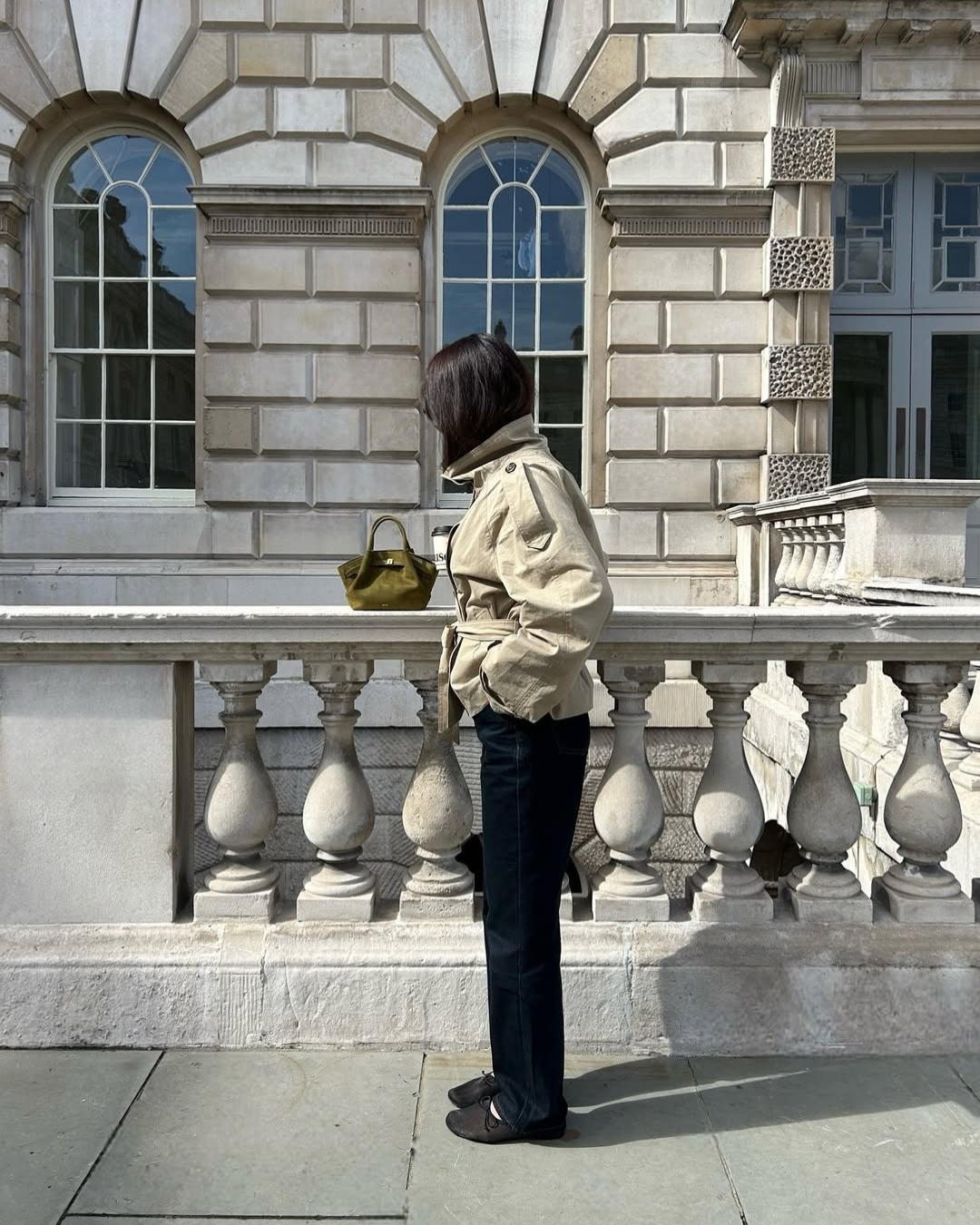 Beige short belted trench coat, model looking at building