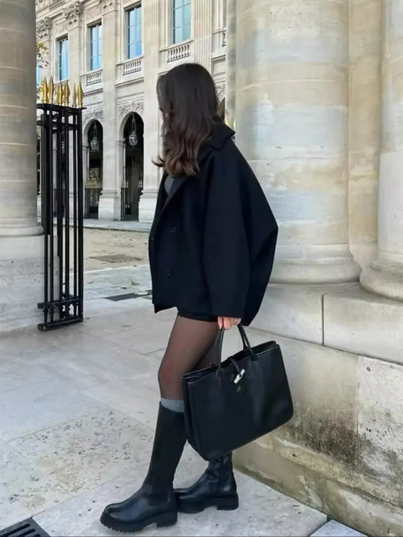 Black oversized coat, side view walking past columns