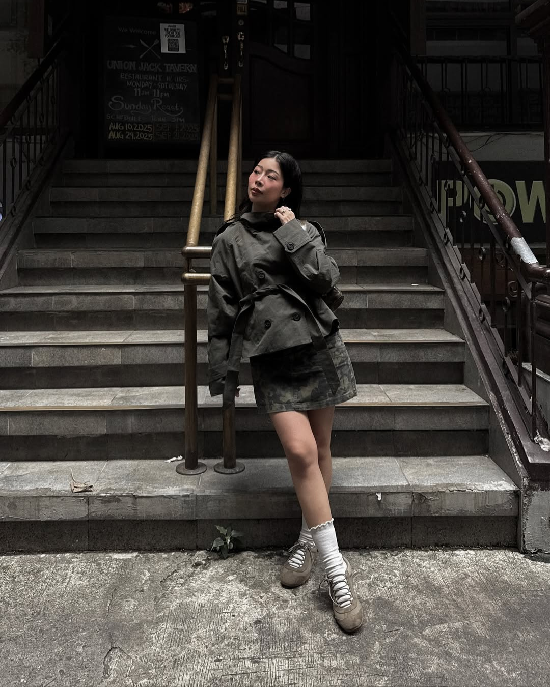Olive green short belted trench coat, model on stairway