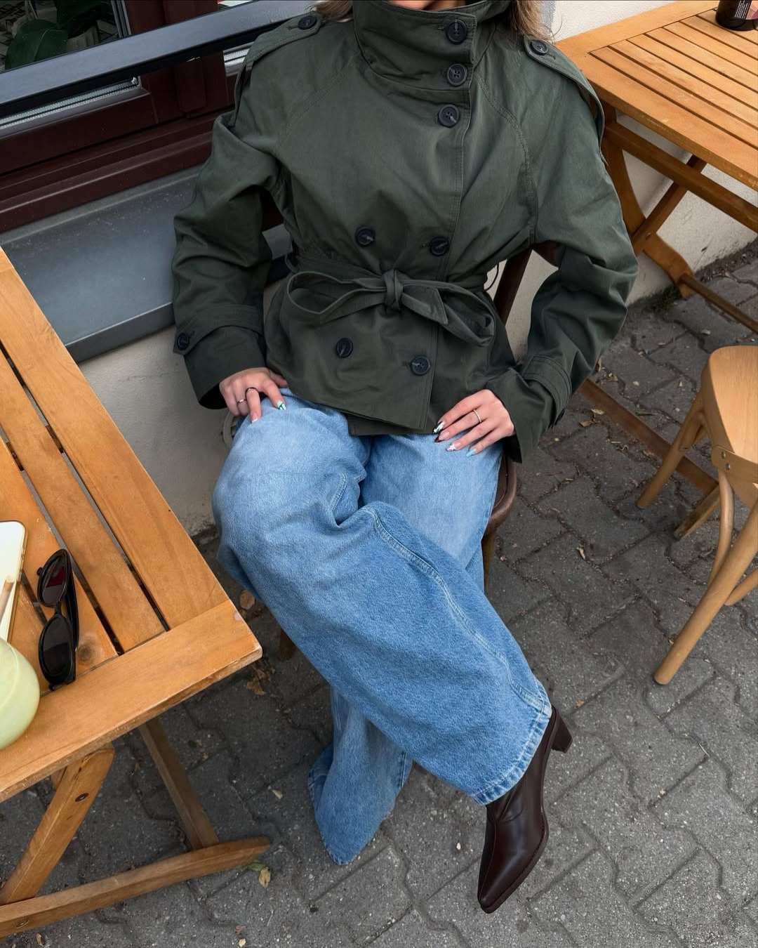 Olive green short belted trench coat, model seated at cafe table