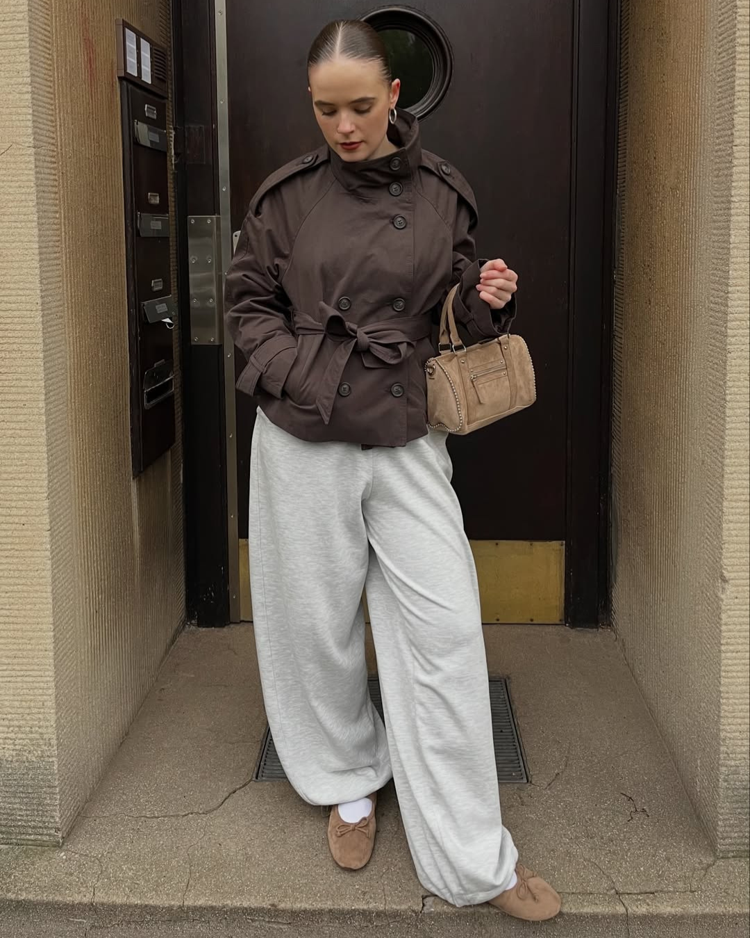 Brown short trench coat with belted waist, model in doorway