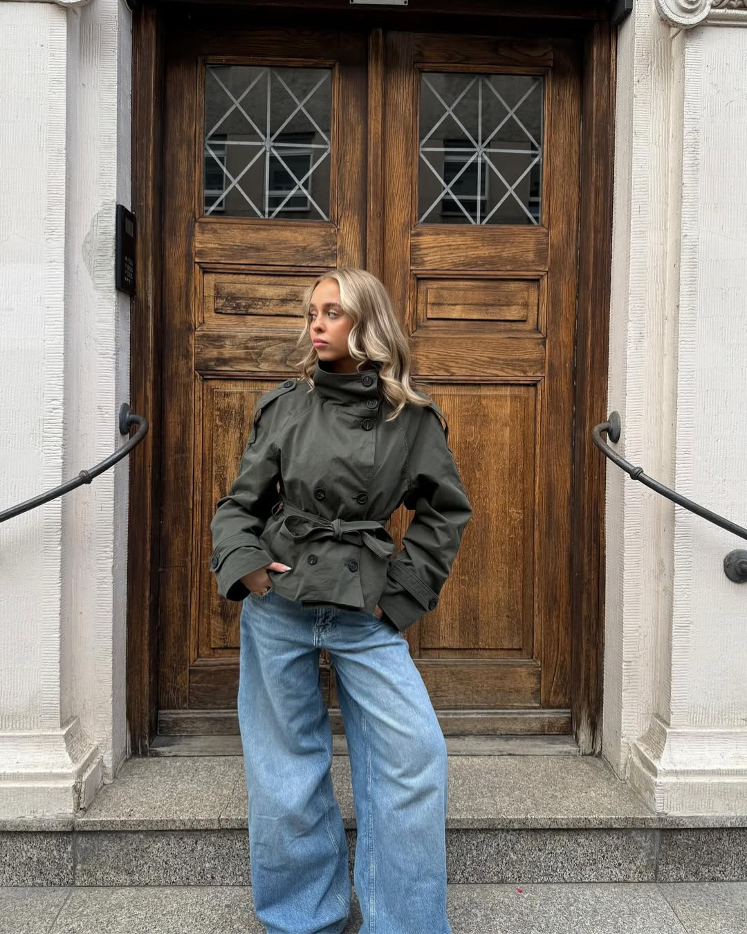 Olive green short belted trench coat, front view on model