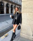 Black oversized coat over white jumper and skirt, front view leaning on column