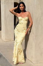 Lemon fitted maxi dress with gold floral embroidery, model against sandstone wall