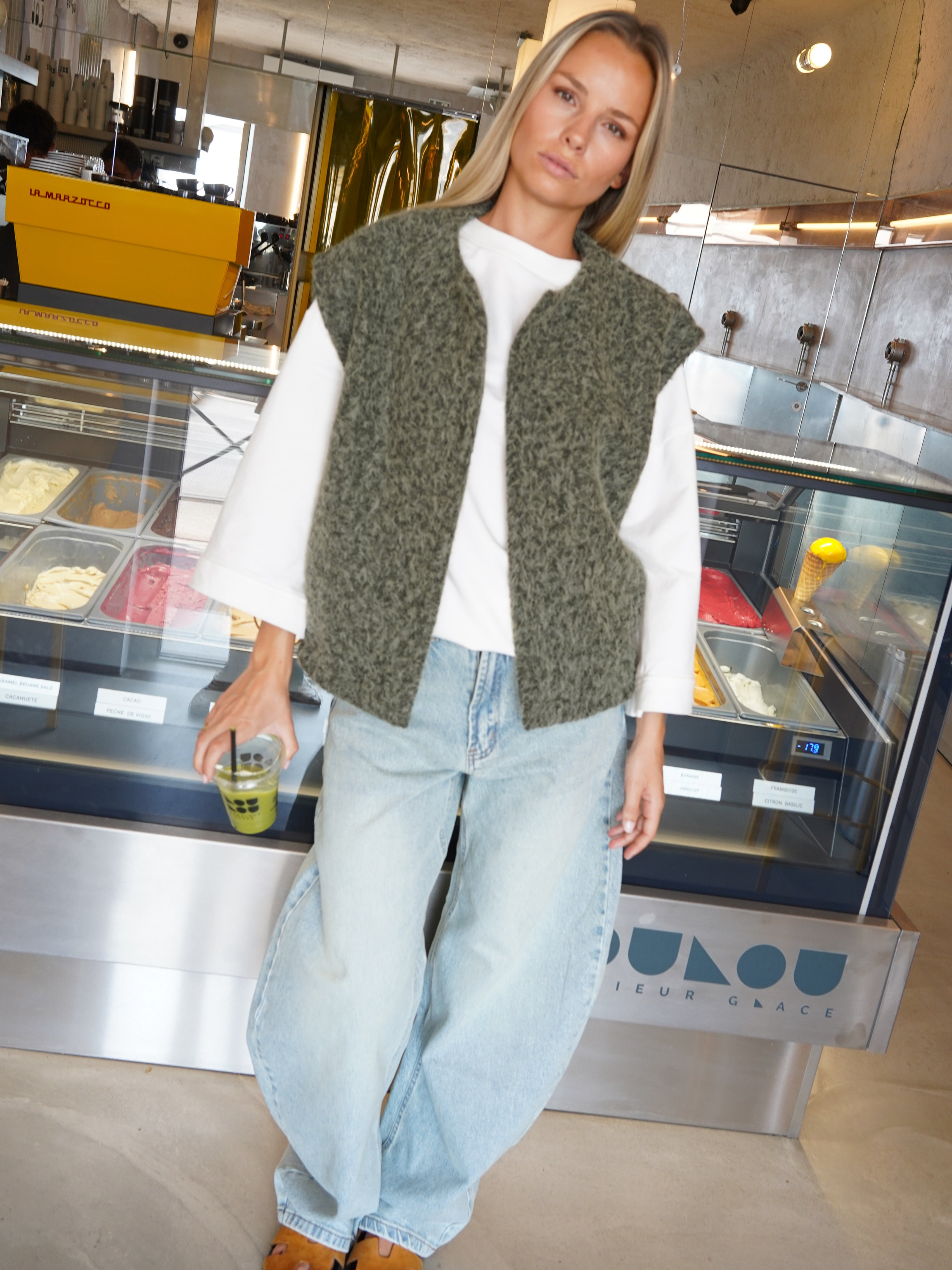 Green bouclé knit vest with jeans, model holding iced drink