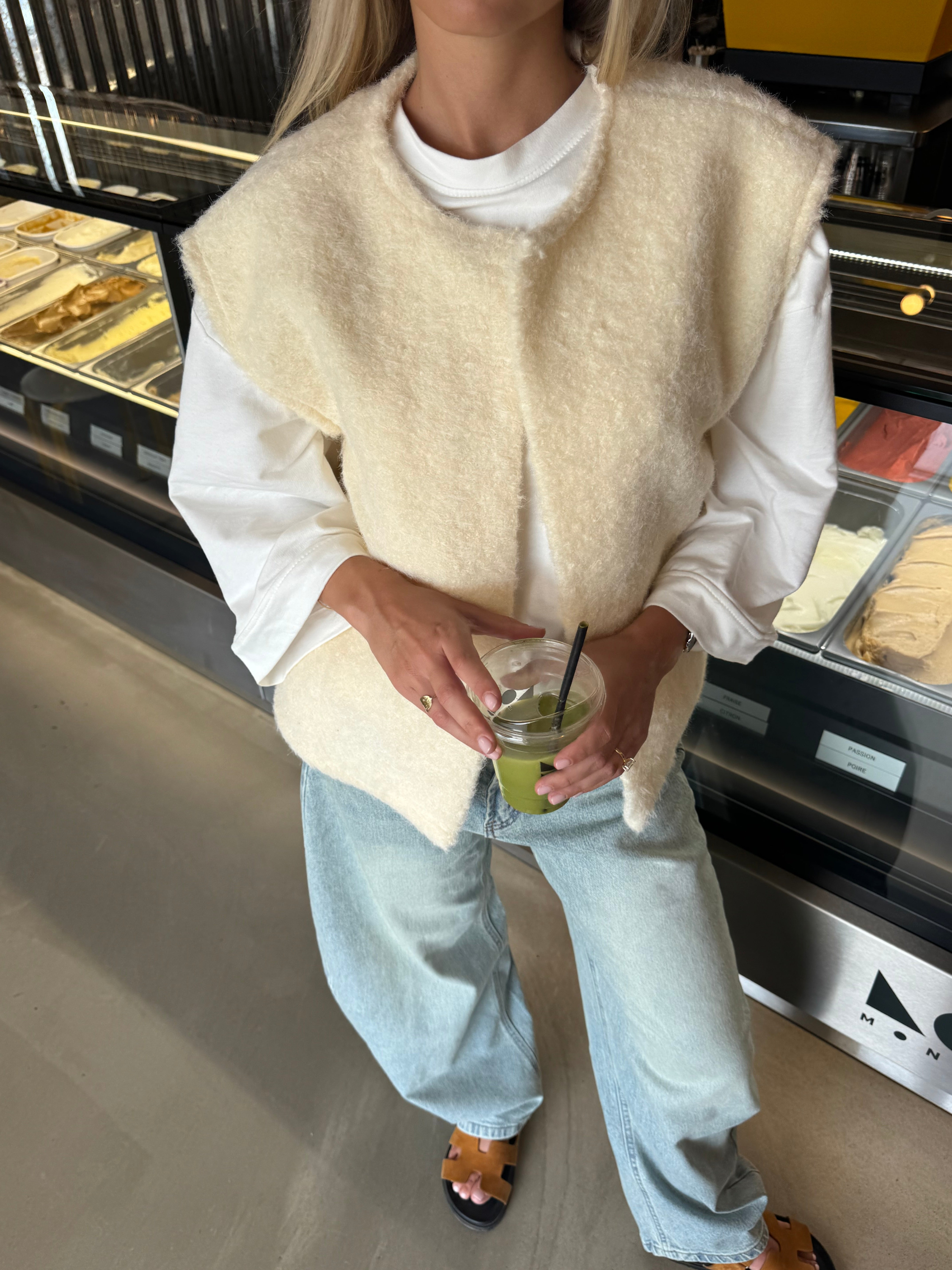 Cream bouclé knit vest with jeans, model holding iced drink