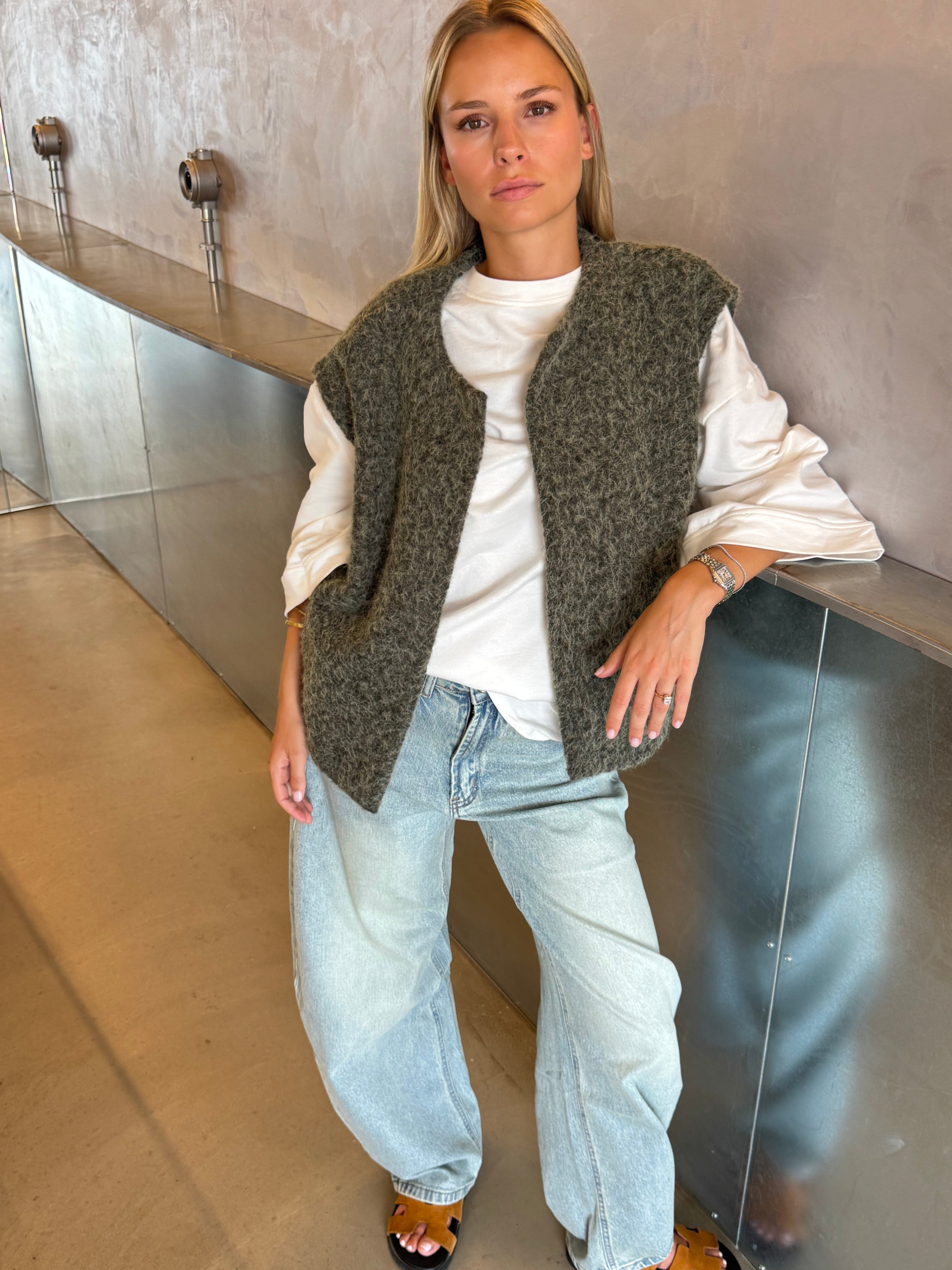 Green bouclé knit vest on model, leaning pose with jeans