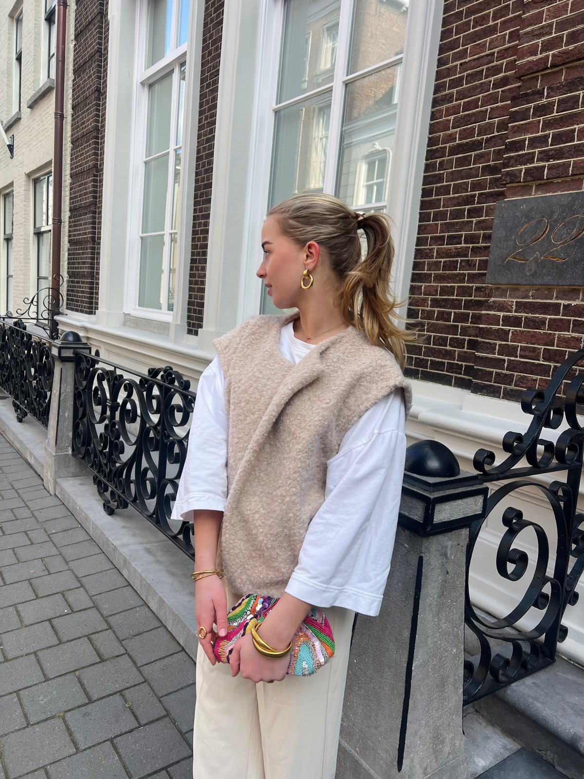 Beige bouclé knit vest over white top on model, side view outdoors