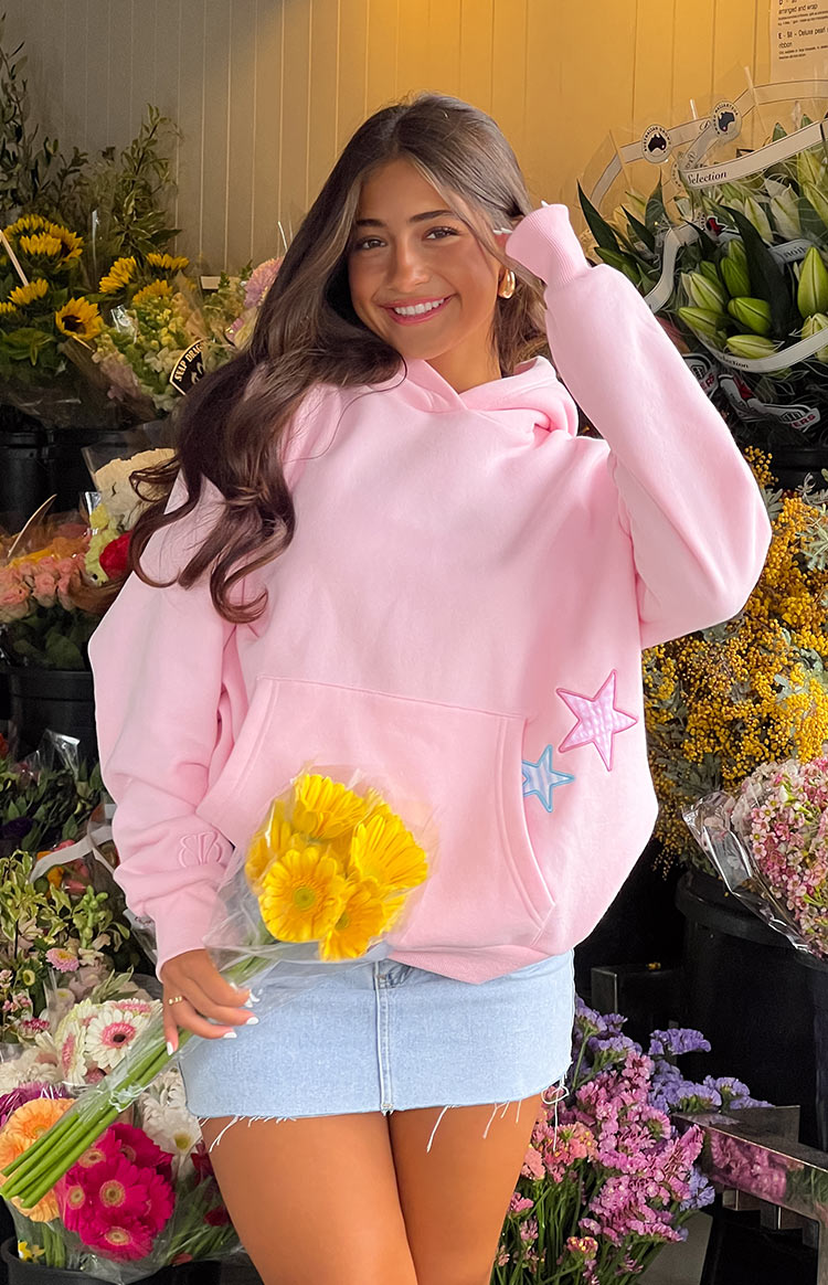 Pink oversized hoodie with star patches, front view on model in flower shop