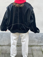 Black oversized contrast-stitch jacket, back view against wall
