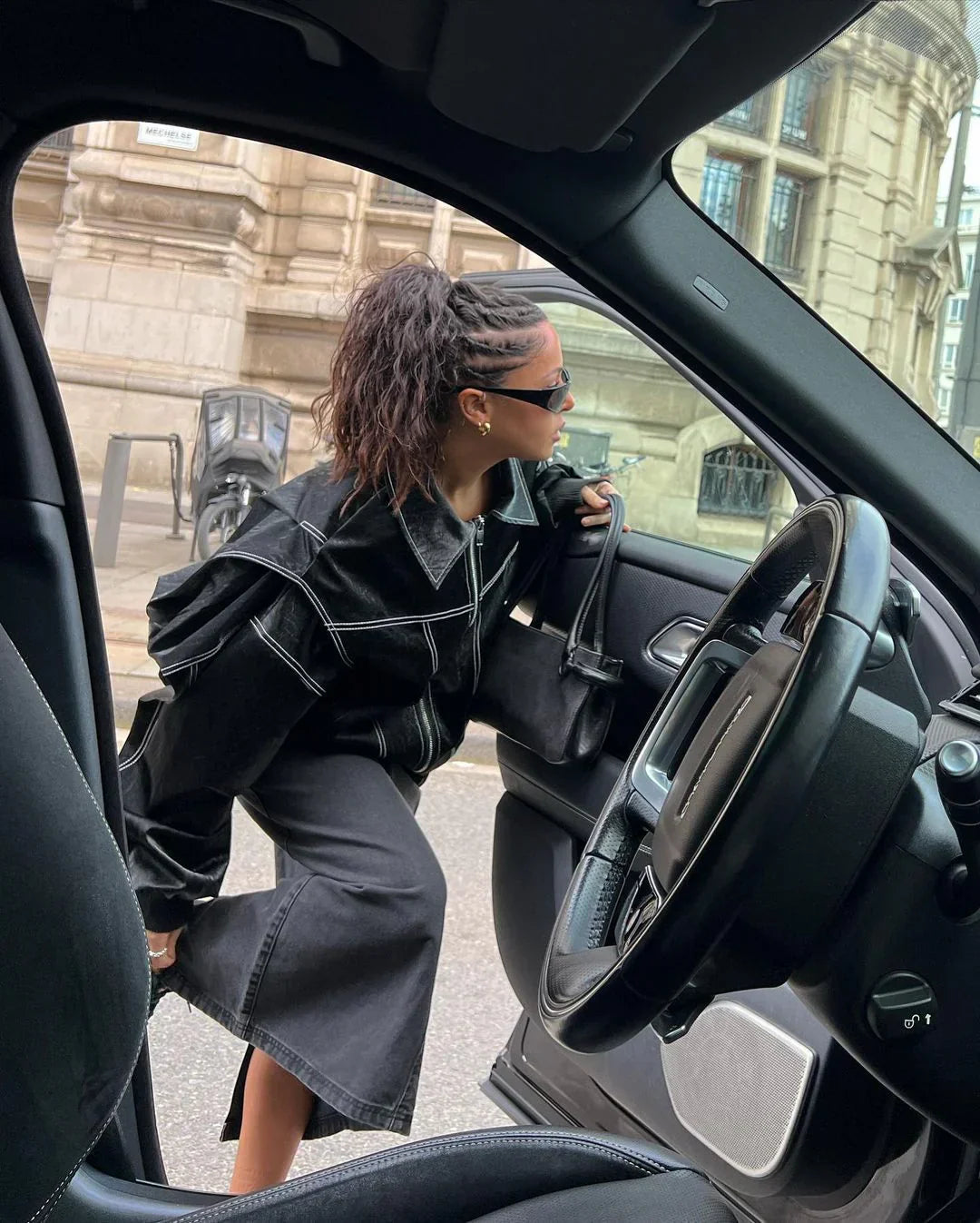 Black oversized contrast-stitch jacket over denim skirt, side view getting into car