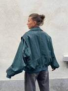 Deep green oversized contrast-stitch jacket, back view against wall