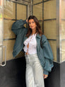 Deep green oversized contrast-stitch jacket, front view by doorway
